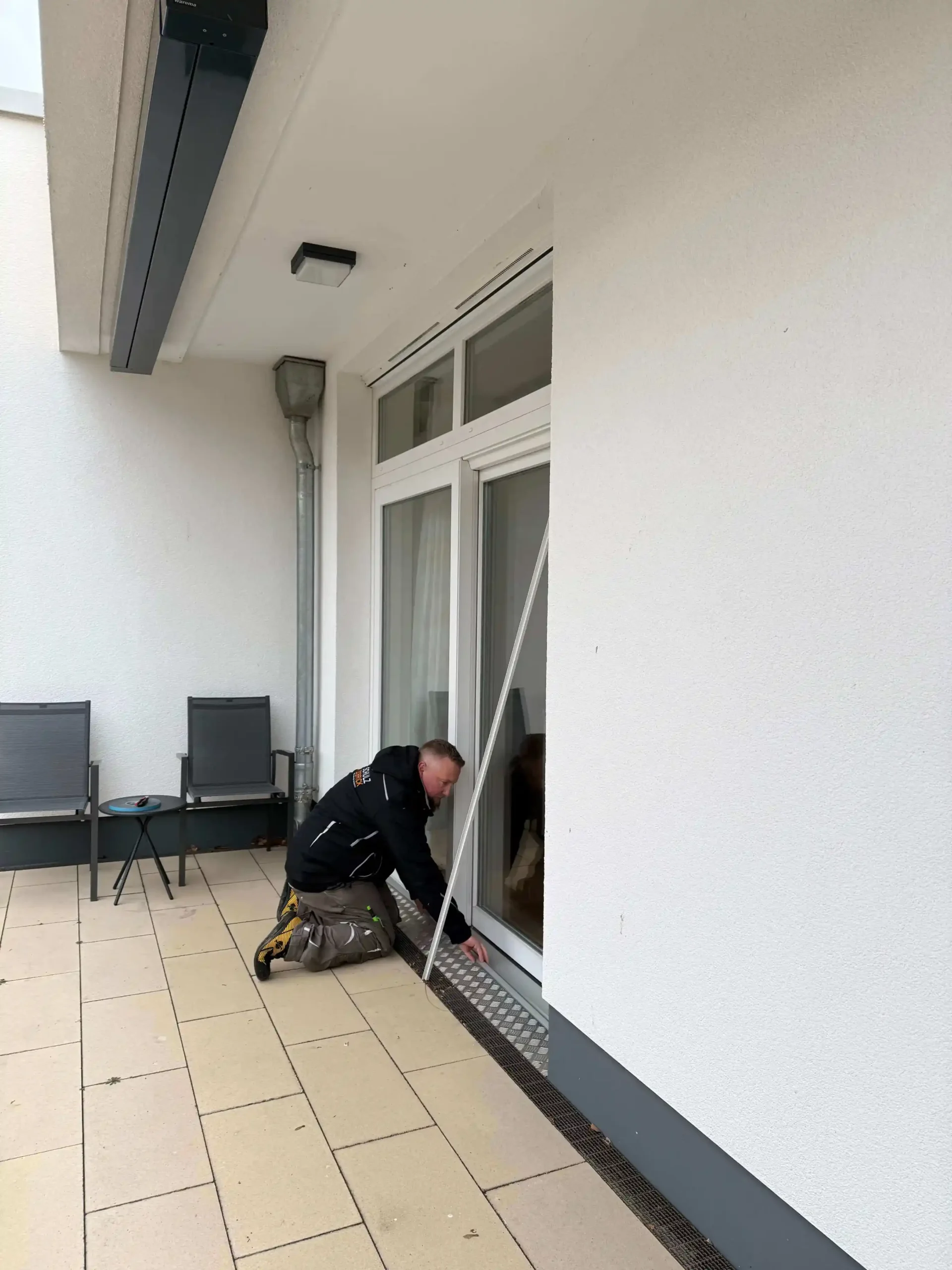 Ein Monteur kniet auf dem Boden und baut eine weiße Insektenschutz-Schiebeanlage ein.