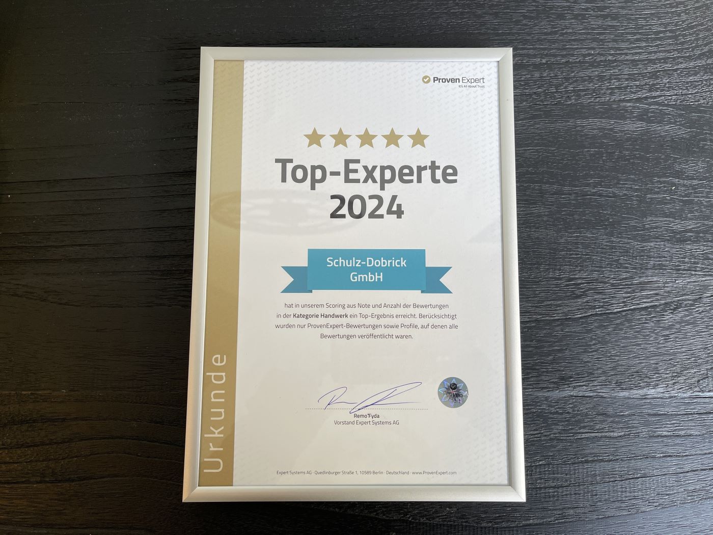 Bilderrahmen liegt auf dunkler Oberfläche, darin Auszeichnung Top-Experte 2024 von Proven Expert für die Schulz-Dobrick GmbH