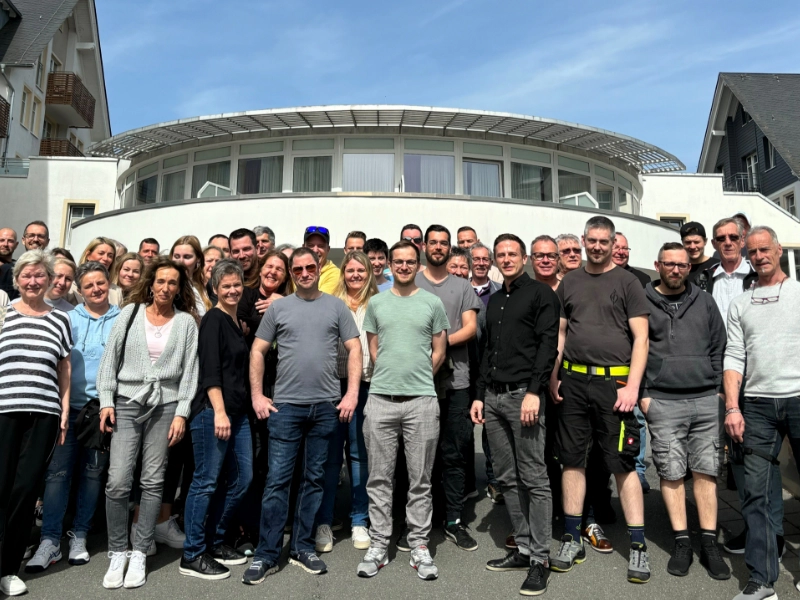 Das Schulz Dobrick Team versammelt sich vor dem Firmengebäude, lächelnd und bereit für ein Gruppenfoto bei sonnigem Wetter.