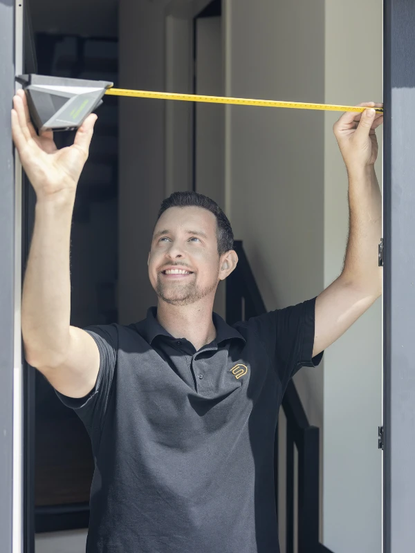 Eine Frau in einem grauen Top öffnet ein Fliegengitter-Fenster in einem hellen Raum.