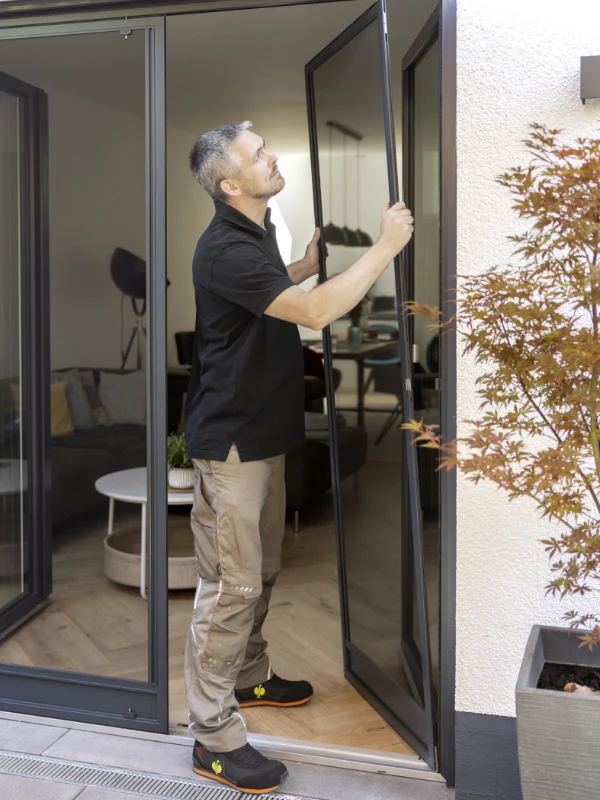 Eine Frau reicht einem Mann durch ein Fenster mit Fliegengitter eine Tasse, während er draußen sitzt.