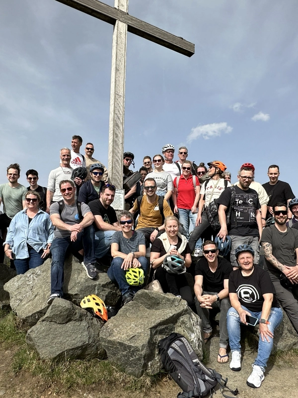 Schulz Dobrick Team posiert bei sonnigem Wetter auf einem Berg neben einem großen Gipfelkreuz.