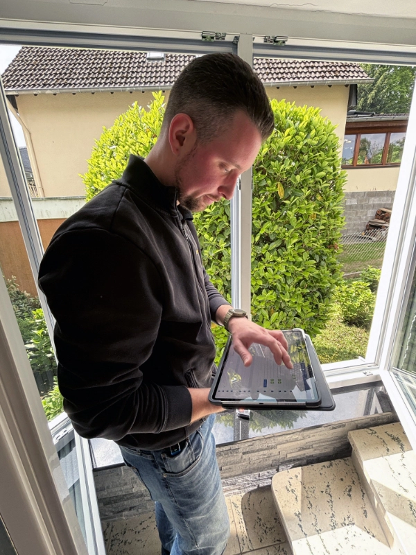 Ein Mitarbeiter von Schulz Dobrick steht an einem geöffneten Fenster und arbeitet auf einem Tablet, um Daten einzugeben.