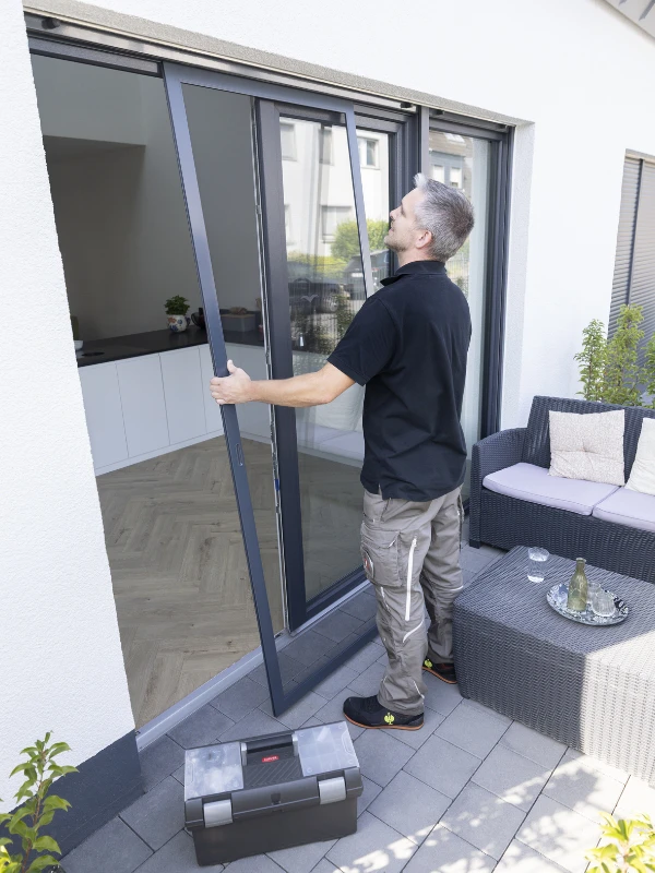 Ein Mann in blauem T-Shirt öffnet ein Fliegengitter an einem Dachfenster in einem modernen Raum.