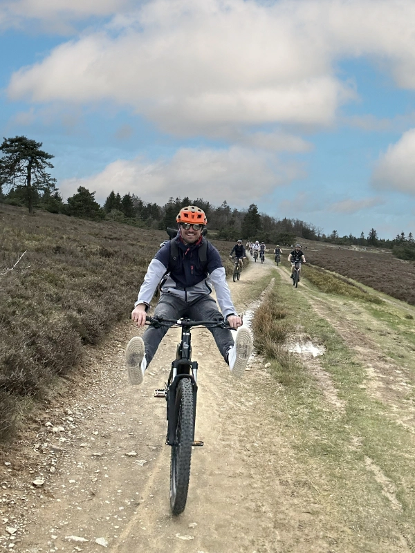Ein Schulz Dobrick Mitarbeiter fährt auf einem Fahrrad über einen Feldweg, mit ausgestreckten Beinen, während er lächelt.